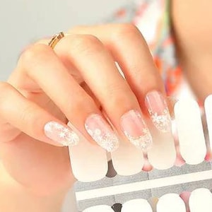May include: A sheet of white nail polish stickers with a glittery design. The stickers are arranged in rows and are ready to be applied to fingernails.