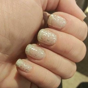 May include: Close-up of a hand with light pink nail polish with a silver glitter design.