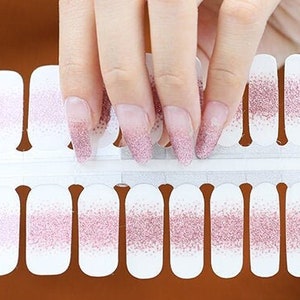 May include: A sheet of pink and white glitter nail polish stickers. The stickers are arranged in rows and columns on a white backing.