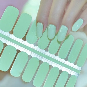 Puede incluir: Una hoja de pegatinas de esmalte de uñas verde claro, con 20 pegatinas individuales de forma rectangular. Las pegatinas están dispuestas en dos filas de diez. Las pegatinas están diseñadas para ser aplicadas en las uñas.