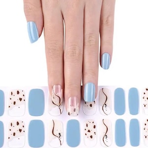 Könnte beinhalten: Eine Folie mit blauen und weißen Nagellack-Stickern mit einem braunen und weißen abstrakten Design. Die Sticker sind mit "NG200224" gekennzeichnet.