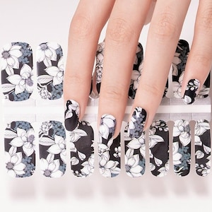 May include: Nail wraps with a floral design in black, white, and grey. The wraps feature a repeating pattern of stylized flowers and leaves. The image shows the nail wraps on a white background, with a hand holding the wraps and some applied to the nails.