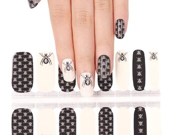 May include: Nail wraps featuring a black and white spider web pattern and spider graphics. The nail wraps are in various shapes and sizes, with some nails painted with a solid off-white color. The nail wraps are designed for easy application.
