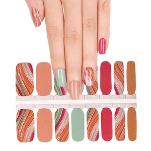 May include: Nail art strips in various colours and designs. The strips include shades of orange, red, green, and brown, with some featuring a wavy pattern and others solid colours. A hand with painted nails is also visible.