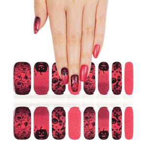 May include: A set of nail polish strips featuring a vibrant red glitter base with black printed designs of jack-o'-lanterns, skulls, ghosts, and swirling filigree patterns. The strips are arranged in multiple sizes on a clear backing sheet.