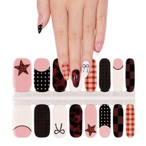 May include: Nail art strips featuring various designs, including a leopard print star, black polka dots, a bow, and a plaid pattern. The strips are in shades of pink, black, and white, with a clear plastic backing. The image also shows a hand with manicured nails.