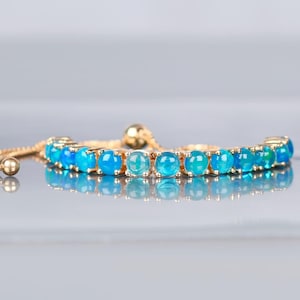 May include: A gold adjustable bracelet with a row of blue opal gemstones. The bracelet has a sliding clasp.