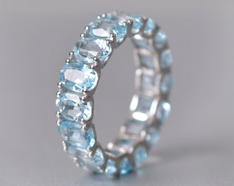 May include: A silver ring with a row of light blue oval-shaped gemstones.