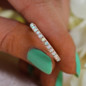 May include: A delicate eternity band ring with a row of white opal stones set in a silver band.
