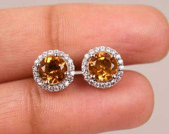 May include: A pair of gold and silver stud earrings with a round, orange gemstone surrounded by a halo of smaller, clear gemstones.