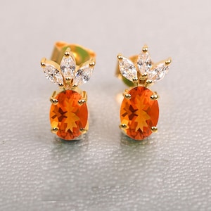 Op de afbeelding: Een paar gouden oorbellen met oranje ovale edelstenen en een kroon van heldere zirkonia-stenen.