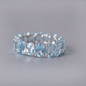 May include: A silver ring with a row of oval-shaped light blue gemstones.