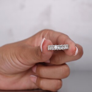 May include: A silver band ring with a row of oval-shaped clear gemstones.