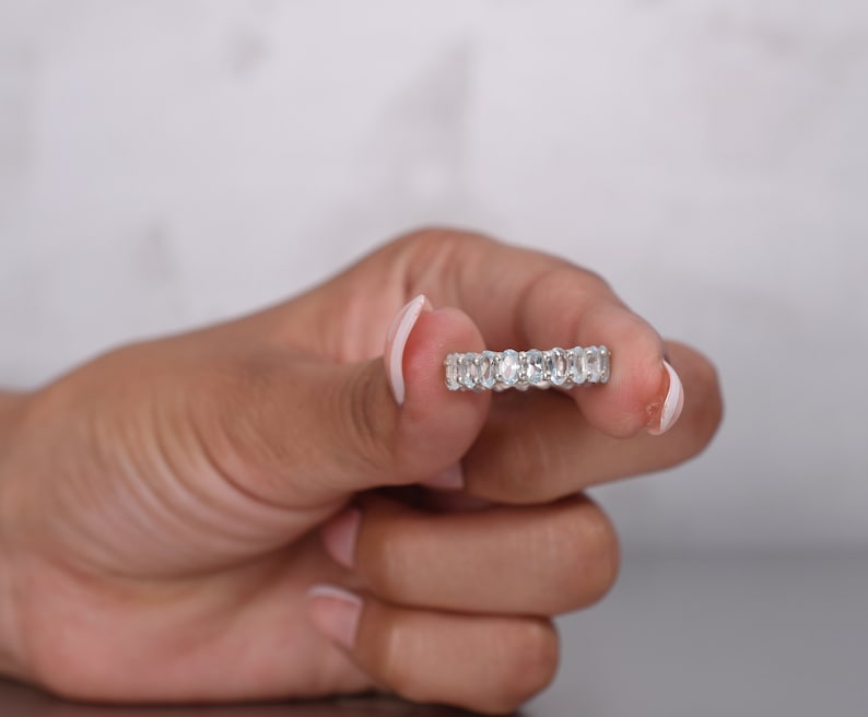 May include: A silver band ring with a row of oval-shaped clear gemstones.