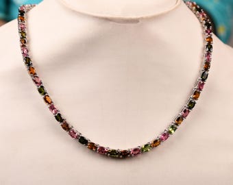 May include: A necklace featuring a series of oval-cut gemstones in shades of pink, green, orange, and brown. The gemstones are set in a silver-colored metal, creating a colorful and elegant piece of jewelry.