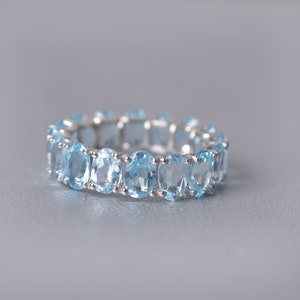 May include: A silver ring with a row of oval-shaped light blue gemstones.
