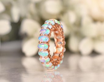 May include: A rose gold eternity band ring with a row of oval-shaped opal gemstones. The ring is set in a delicate, prong setting.