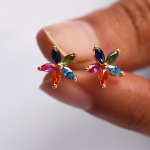 Puede incluir: Un par de pendientes de oro en forma de flor con piedras preciosas de colores. Los pendientes tienen un diseño de flor de cinco pétalos, con cada pétalo engastado con una piedra preciosa de color diferente.