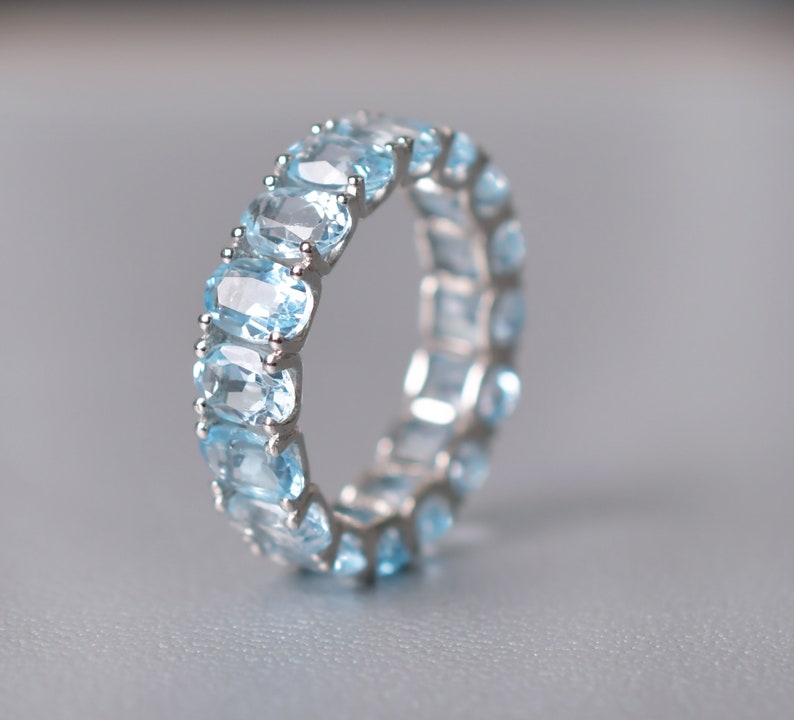 May include: A silver ring with a row of oval-shaped light blue gemstones.