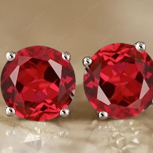 Könnte beinhalten: Ein Paar silberne Ohrstecker mit runden, roten Edelsteinen.