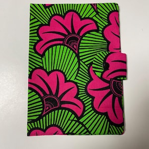 Puede incluir: Una funda de tela rectangular con un patrón vibrante de grandes flores rosas con contornos negros sobre un fondo verde lima brillante con líneas negras radiantes. La funda incluye una pequeña pestaña lateral con un cierre de botón a presión negro.