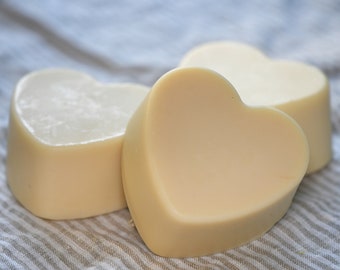 Może przedstawiać: Trzy serduszka z mydła, wykonane z naturalnych składników, ułożone na tle wzorzystej tkaniny. Mydło jest jasnobeżowe.