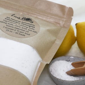 K&ouml;nnte beinhalten: Ein brauner Papierbeutel gef&uuml;llt mit wei&szlig;em Pulver mit der Aufschrift "Corn's Bolly All Natural Automatic Dishwasher Detergent". Die Zutaten sind aufgelistet: Waschsoda, Backsoda, Zitronens&auml;ure, Meersalz und &auml;therisches Zitronen&ouml;l. Der Beutel befindet sich neben einer kleinen Sch&uuml;ssel mit wei&szlig;em Pulver und zwei Zitronen.