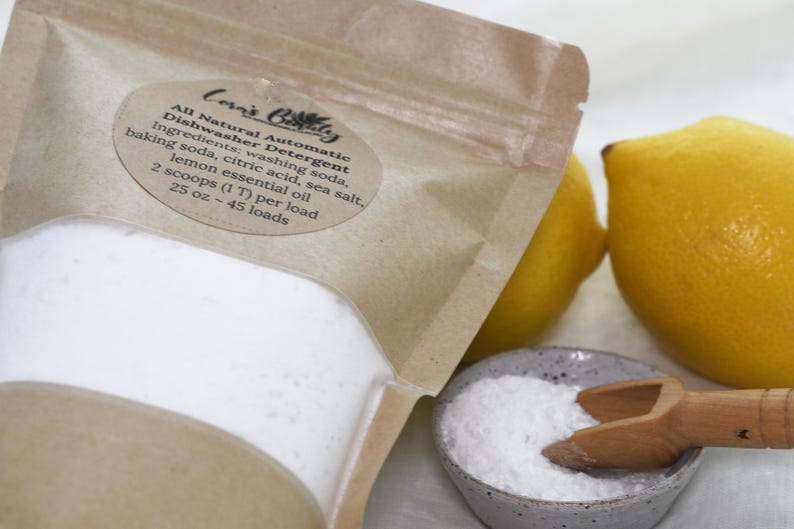 K&ouml;nnte beinhalten: Ein brauner Papierbeutel gef&uuml;llt mit wei&szlig;em Pulver mit der Aufschrift "Corn's Bolly All Natural Automatic Dishwasher Detergent". Die Zutaten sind aufgelistet: Waschsoda, Backsoda, Zitronens&auml;ure, Meersalz und &auml;therisches Zitronen&ouml;l. Der Beutel befindet sich neben einer kleinen Sch&uuml;ssel mit wei&szlig;em Pulver und zwei Zitronen.