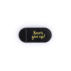Op de afbeelding: Zwarte webcam-afdekking met de tekst "Never give up!" in gele letters.