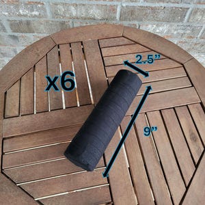 May include: Six black foam rollers, each measuring 9 inches long and 2.5 inches in diameter. The rollers are on a wooden table.