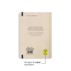 May include: A beige notebook with the text "Coverdesign by dinosaurus.art" and a "VEGAN" label. The notebook is made of grass paper and has text in English and German. The text describes the notebook as vegan and biodegradable.