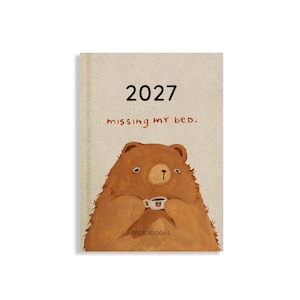 May include: A beige planner with the text 2027 and missing my bed. printed on the cover. The illustration features a brown bear holding a small white mug with a bear face on it. The word motabooks is printed in small black letters at the bottom.