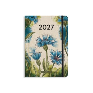 Può includere: Un'agenda 2027 con copertina color crema caratterizzata da un'illustrazione ad acquerello di fiordalisi blu con steli e foglie verdi. Il design include schizzi di vernice verde e blu e un elastico nero chiude lateralmente il taccuino.