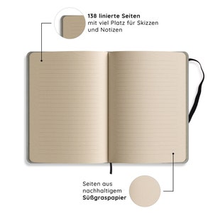 May include: Open notebook with lined pages. The pages are a light tan color, and the cover is a muted gray. The notebook has a black ribbon bookmark. Text on the image reads: "138 lined pages with plenty of space for sketches and notes."