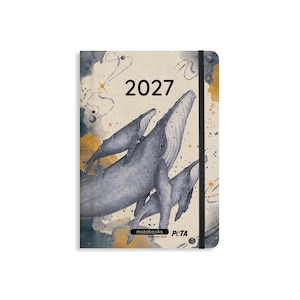 May include: A 2027 planner with a cream-colored cover featuring a watercolor illustration of three blue whales swimming among gold and dark blue abstract shapes, stars, and planets. A black elastic band secures the notebook, which includes the text matabooks together with PETA.