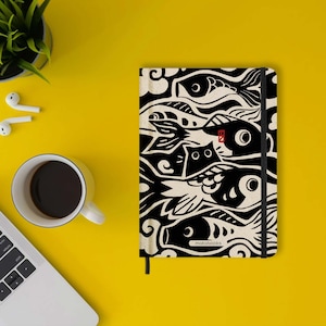 Peut inclure: Un carnet noir et blanc avec un motif de poisson. La couverture présente un motif abstrait de poissons et d'autres éléments aquatiques. Le carnet a une fermeture élastique noire et le mot "motobooks" est imprimé en bas.