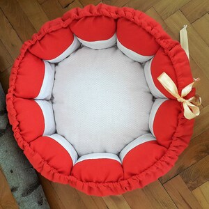 May include: A red and white round pet bed with a white center and red outer rim. The bed has a decorative bow on the side.