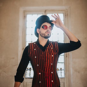 May include: A man wearing a black top hat, red-tinted round glasses, a black long-sleeved shirt, and a red and black striped vest with silver buttons. The vest has a pointed collar and a fitted silhouette.