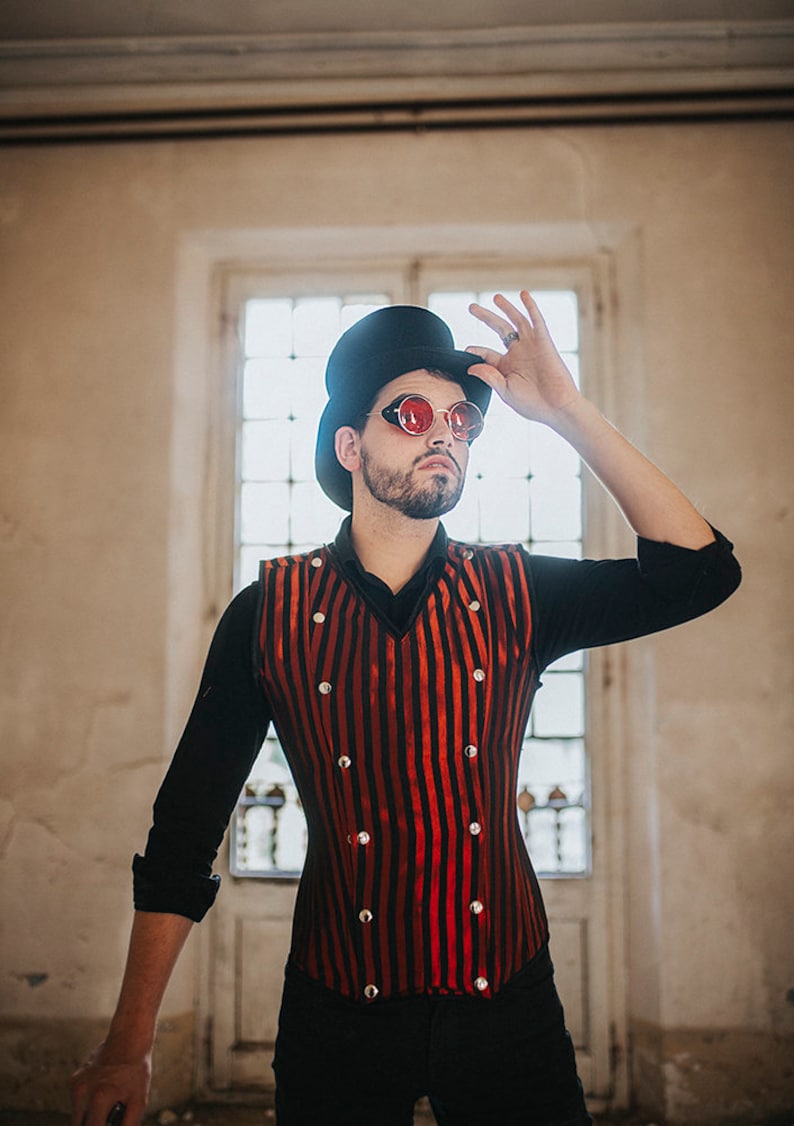 May include: A man wearing a black top hat, red-tinted round glasses, a black long-sleeved shirt, and a red and black striped vest with silver buttons. The vest has a pointed collar and a fitted silhouette.