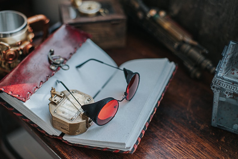May include: A red leather-bound journal with a compass and a pair of black steampunk-style glasses with red lenses.