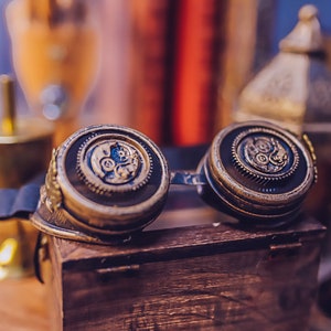 Puede incluir: Un par de gafas de estilo steampunk con monturas de color lat&oacute;n y detalles intrincados en forma de engranajes. Las gafas est&aacute;n apoyadas en una caja de madera.