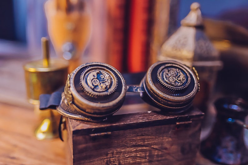 Puede incluir: Un par de gafas de estilo steampunk con monturas de color lat&oacute;n y detalles intrincados en forma de engranajes. Las gafas est&aacute;n apoyadas en una caja de madera.