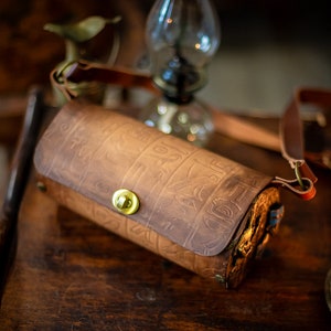 May include: A brown leather cylindrical bag with an embossed design and a brass clasp. The bag has a long brown leather strap.