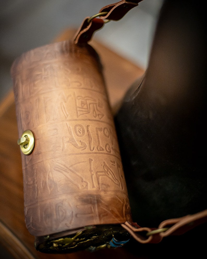 May include: A brown leather bag with a strap and a gold clasp. The bag is decorated with an embossed pattern.