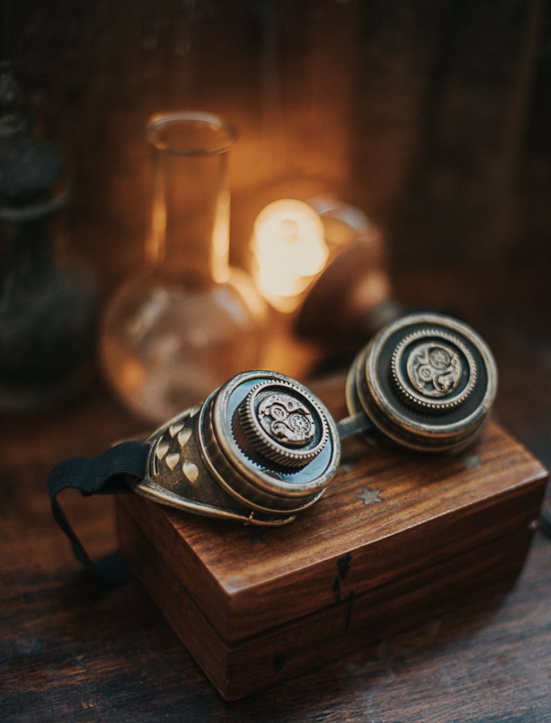Puede incluir: Un par de gafas steampunk con detalles en lat&oacute;n y una correa negra. Las gafas est&aacute;n sobre una caja de madera con un dise&ntilde;o de estrella.