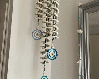 May include: A handmade, cream-colored crochet spiral mobile with turquoise and beige accents. The mobile features three decorative crochet medallions in shades of blue and beige, and wooden beads. It hangs from a wooden dowel.