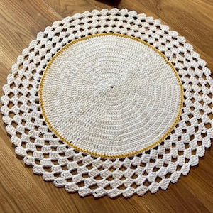 May include: Two-piece, handmade, white crochet doilies. The top doily is a solid circle with a yellow border, and the bottom doily has a scalloped edge with openwork. The doilies are on a wooden surface.