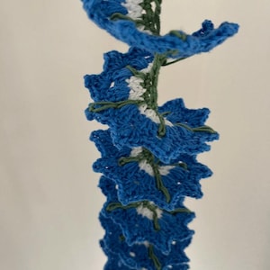 May include: A crocheted garland of blue, white, and green flowers. The garland is made of yarn and is strung together with a green thread.