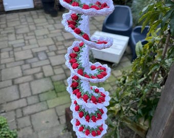 May include: A white crocheted spiral with red and green accents. The spiral is hanging from a hook and is made of yarn.