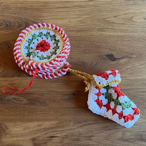 Op de afbeelding: Gehaakte kerstornamentenset met een ronde onderzetter en een kleine kous. De onderzetter heeft een rood, wit en groen ontwerp met een rood centrum. De kous is wit met rode en groene accenten en een gouden rand.